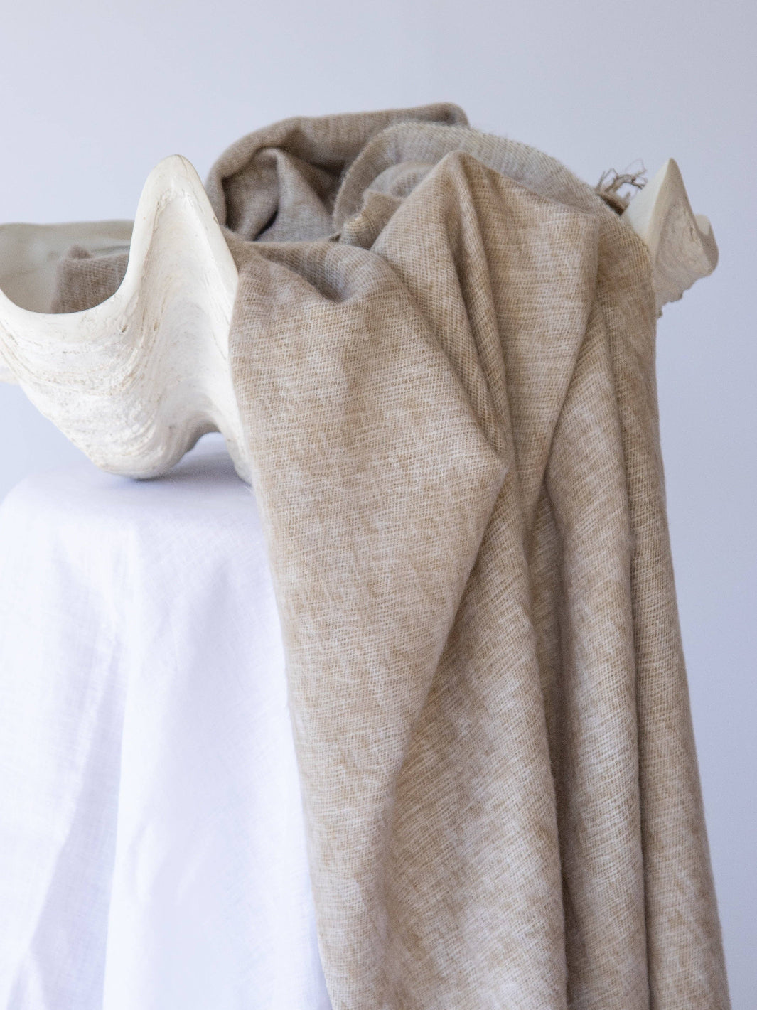Beige shawl draped over a white surface with a neutral background