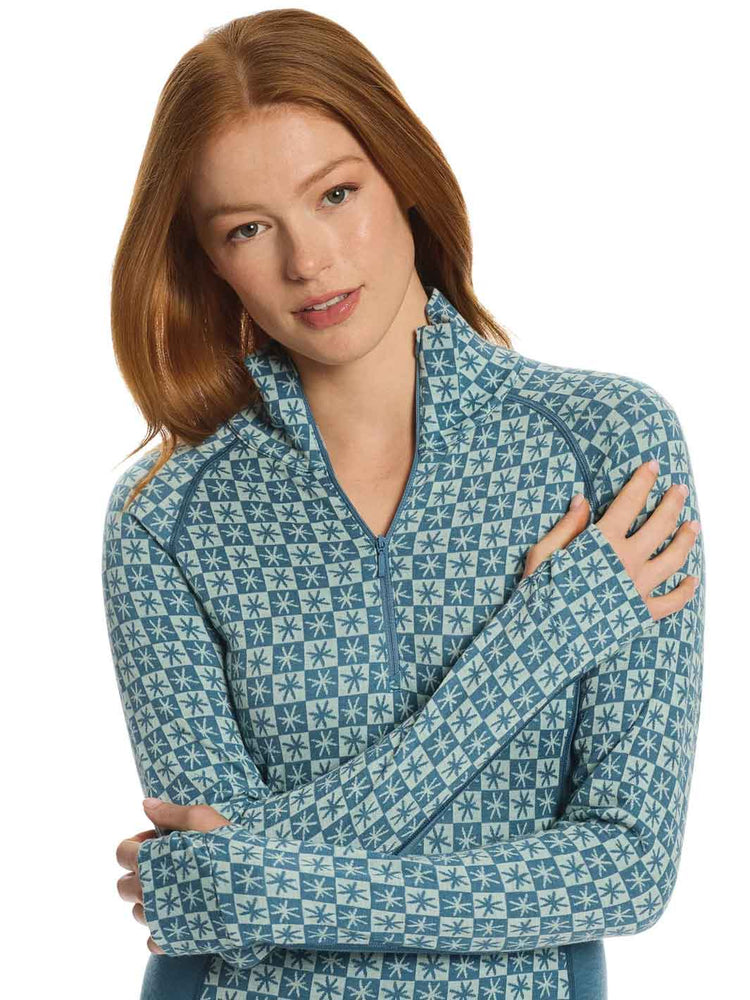 A woman with red hair wearing a blue and white patterned quarter-zip fleece jacket, posed with her arms crossed against a solid white background.