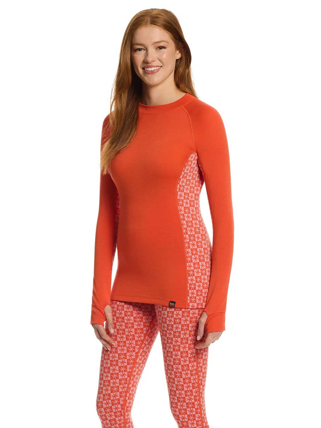A woman modeling a long-sleeve athletic top and matching patterned leggings set in a bright orange-red color, shown against a plain white background.