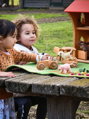 Two children playing with felt animal toys on a wooden table outdoors.
