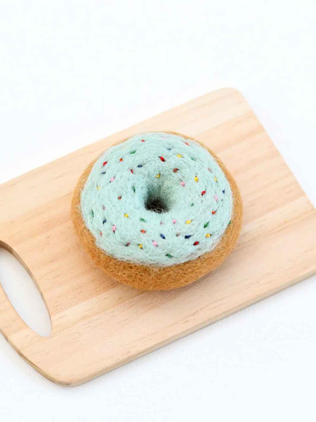 Felted turquoise donut toy with sprinkles on a wooden board