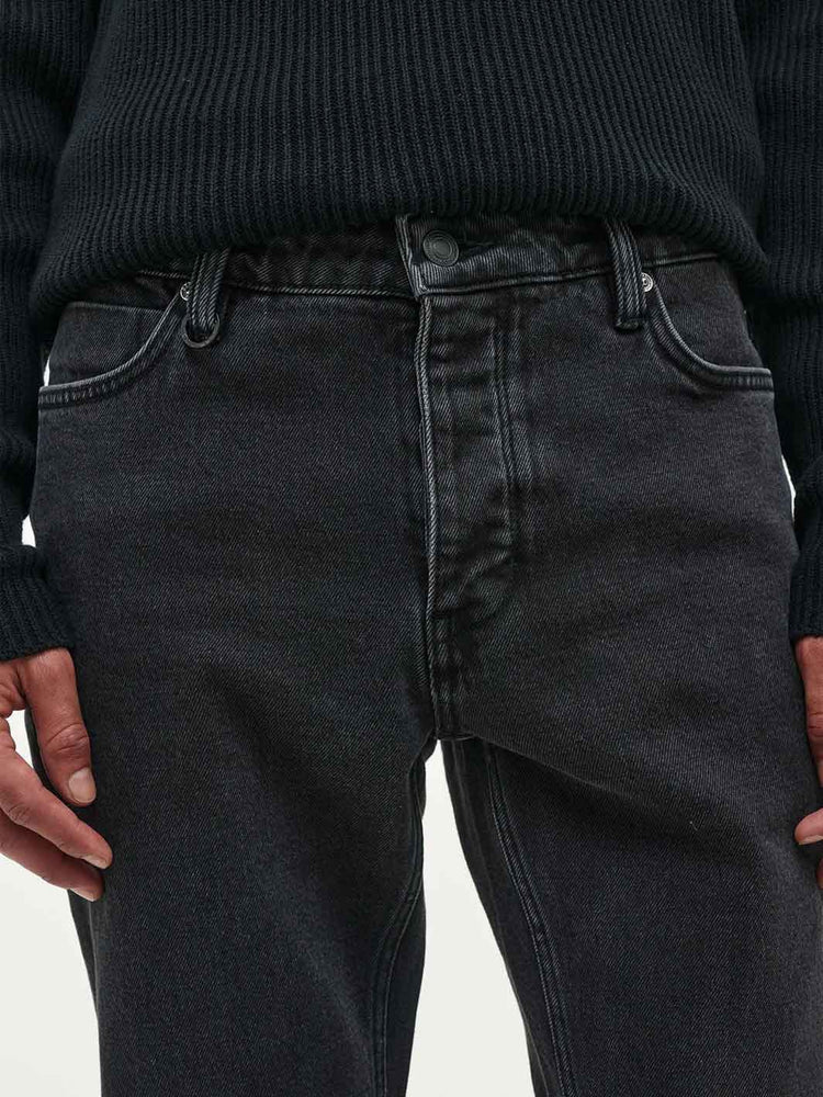 Close-up of a person wearing dark washed black denim jeans and a black ribbed sweater, showing the waistband, front pockets, and hands.