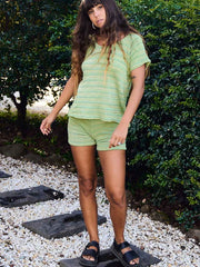 Person wearing a green striped outfit standing outdoors on a pebbled surface with greenery in the background.