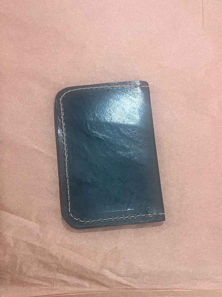 A small black leather card holder or wallet with brown contrast stitching, lying on a textured pink surface.