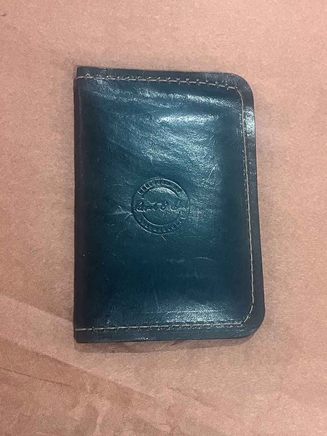 A black leather small wallet with visible brown stitching and an embossed circular logo&