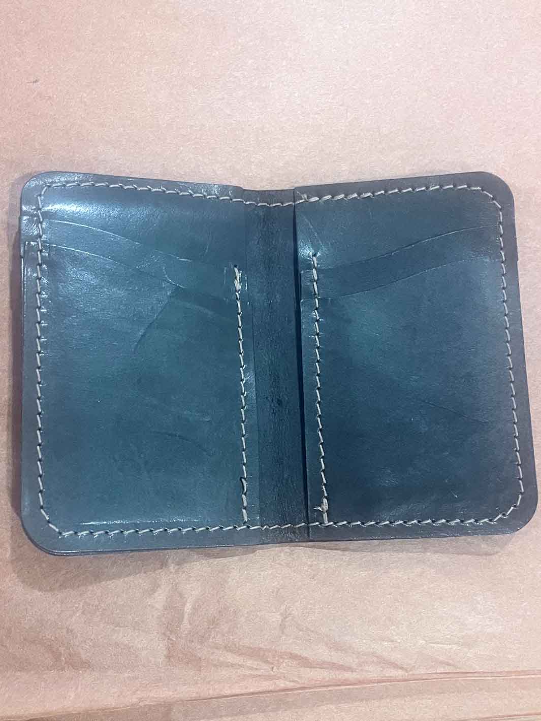 An open black leather wallet with brown stitching, showing multiple card slots and interior pockets, photographed on a light brown paper background.