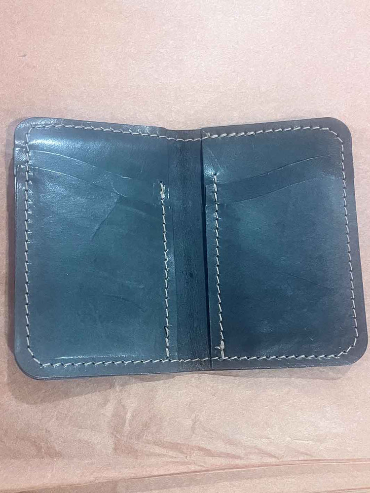 An open black leather wallet with brown stitching, showing multiple card slots and interior pockets, photographed on a light brown paper background.