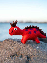 Red toy dinosaur with brown spikes on a rock by a body of water