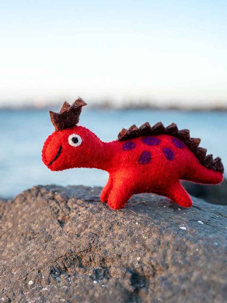 Red toy dinosaur with brown spikes on a rock by a body of water