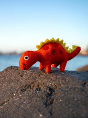 Red dinosaur toy with yellow spikes on a rock by a body of water