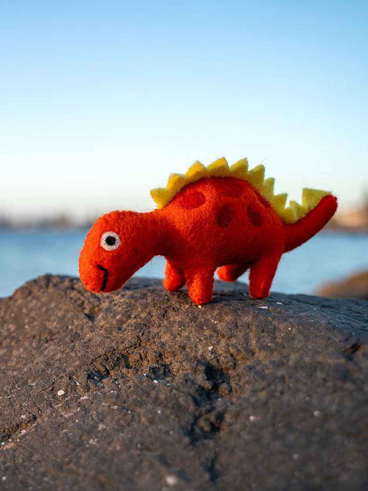 Red dinosaur toy with yellow spikes on a rock by a body of water