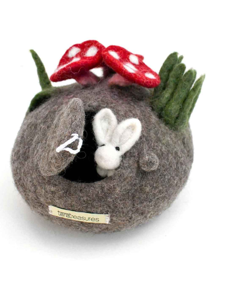 Felted animal toy with a mouse inside a stone, surrounded by grass and red mushrooms on a white background.