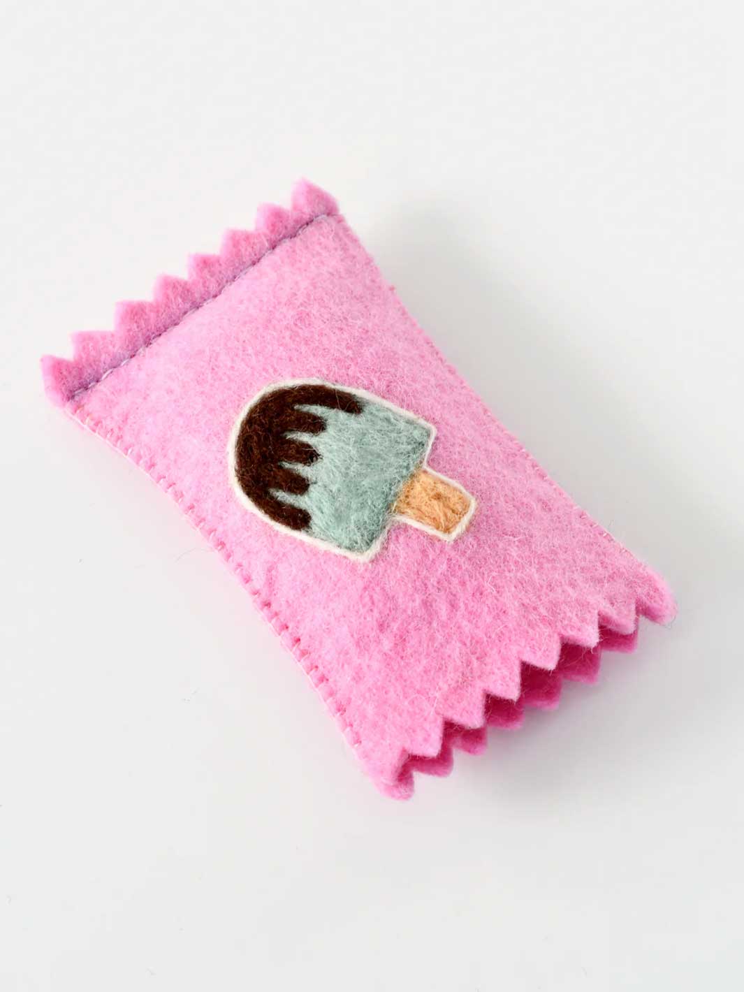 A pink felt accessory with a scalloped edge and an embroidered popsicle patch in the center, shown on a plain light background.