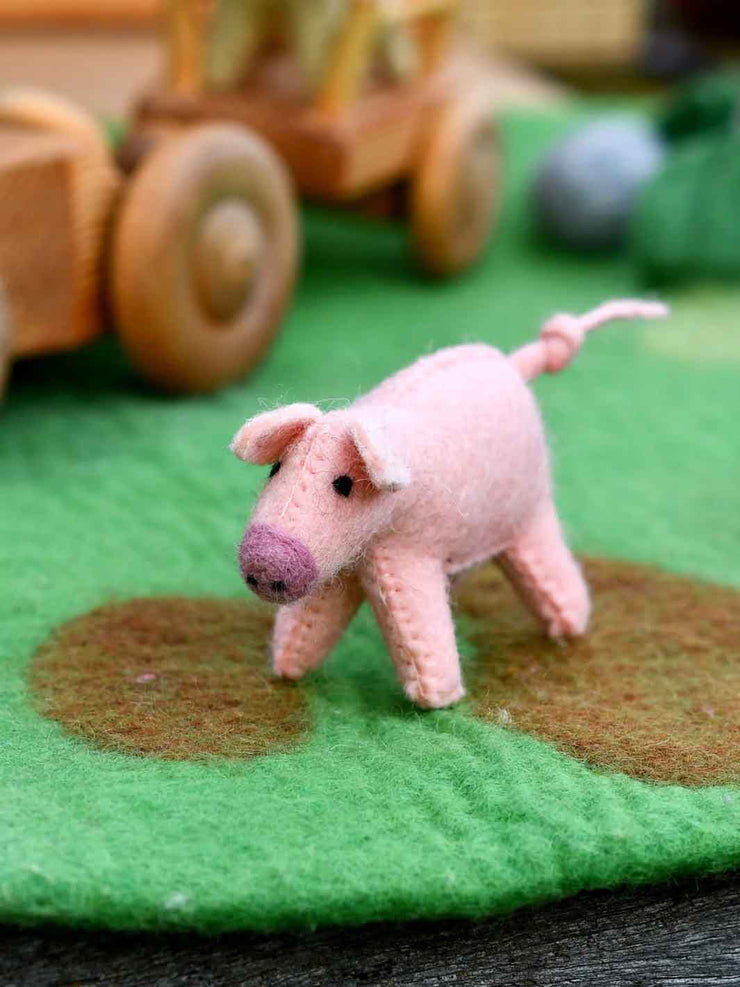 Small pink felt pig toy on a green surface with blurred wooden toys in the background