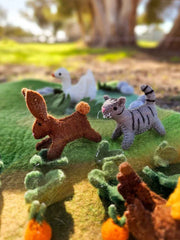 Felt animal toys on a green felt landscape with trees in the background