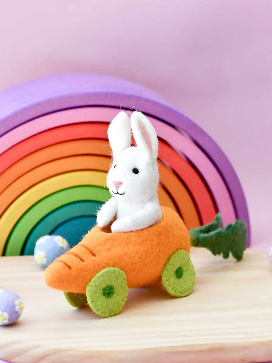 White rabbit plush toy in a carrot car with a colorful rainbow in the background