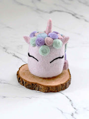 Pastel-colored plush toy with a floral crown on a wooden stand against a marble background