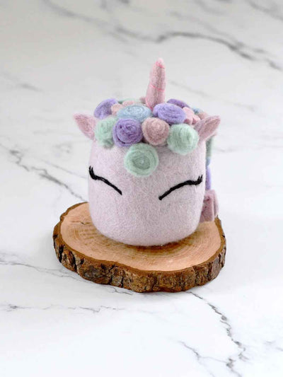 Pastel-colored plush toy with a floral crown on a wooden stand against a marble background