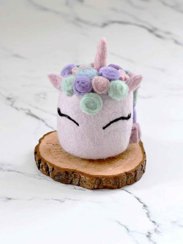 Pastel-colored plush toy with a floral crown on a wooden stand against a marble background