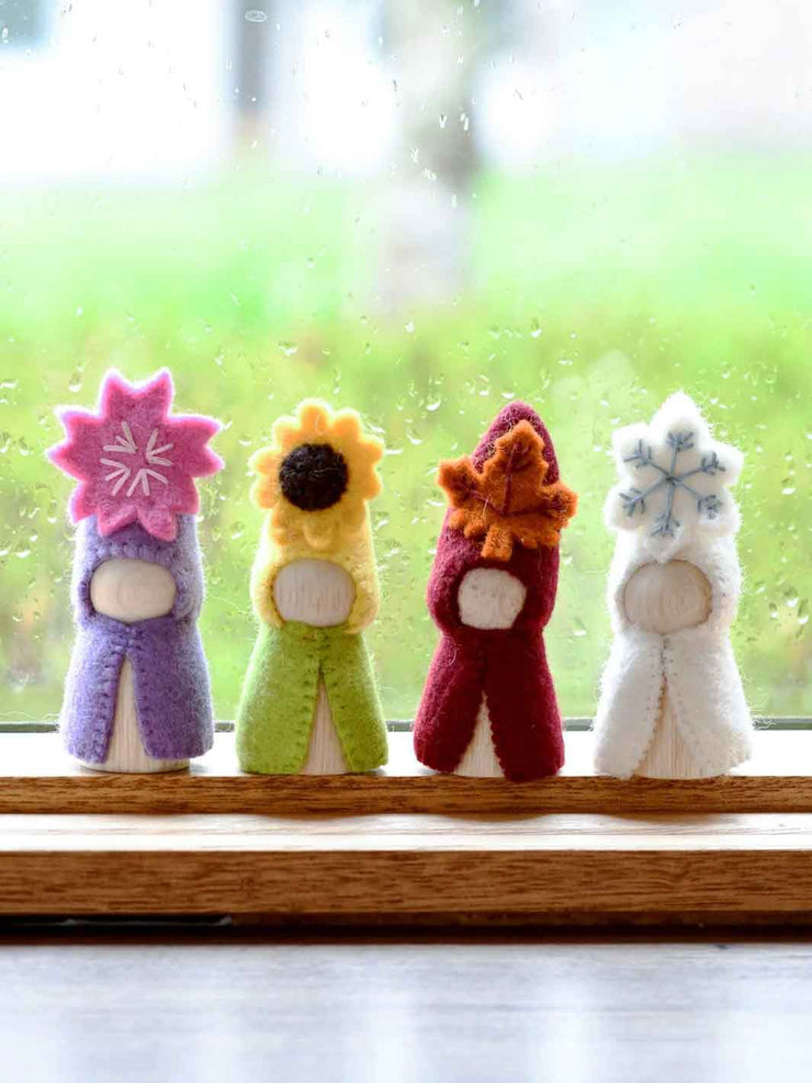Four colorful felt flower dolls on a windowsill with a blurred green garden background.