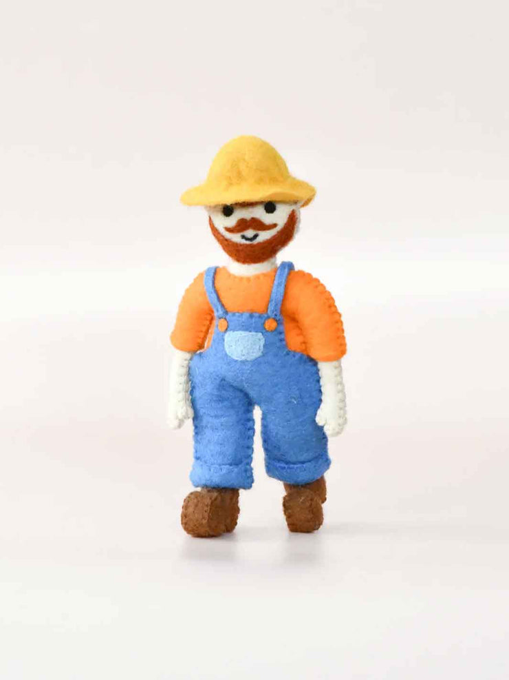 Felt toy figure of a person wearing an orange shirt, blue overalls, and a yellow hat on a white background.