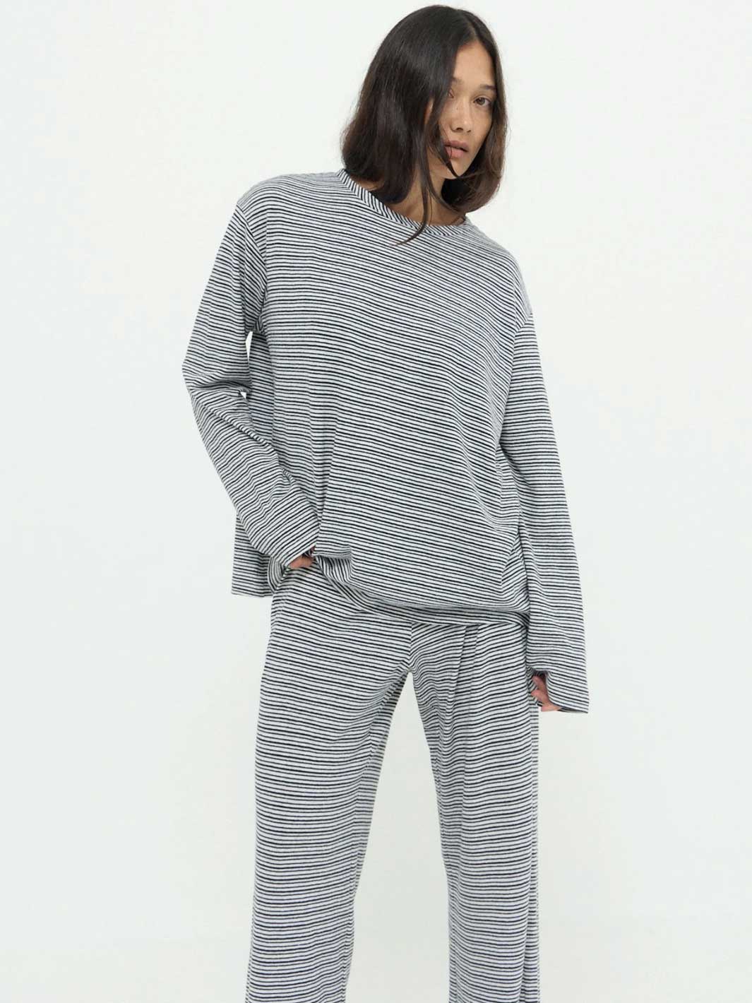 A woman modeling a matching two-piece loungewear set consisting of a long-sleeve crewneck top and wide-leg pants, both featuring a fine horizontal stripe pattern in gray and white.