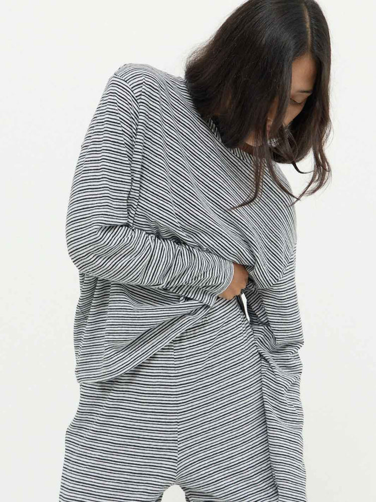 A woman wearing a loose, long-sleeve striped lounge set in gray and white, shown from the side against a plain white background.