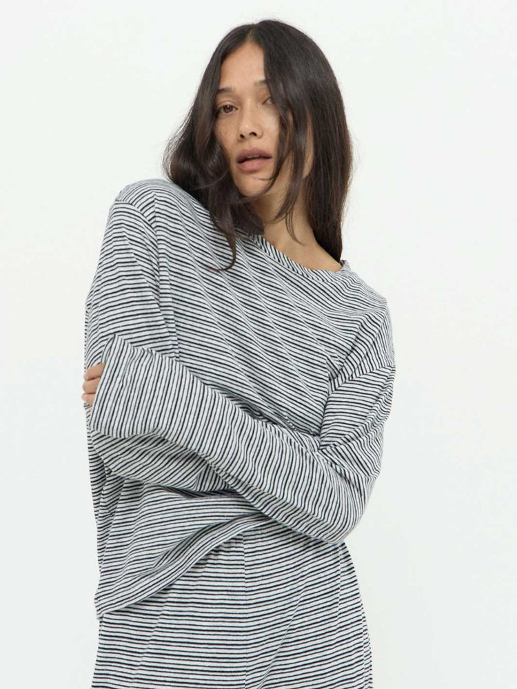 A woman wearing a loose, long-sleeve striped top with thin black and white horizontal stripes, posed against a plain white studio background.