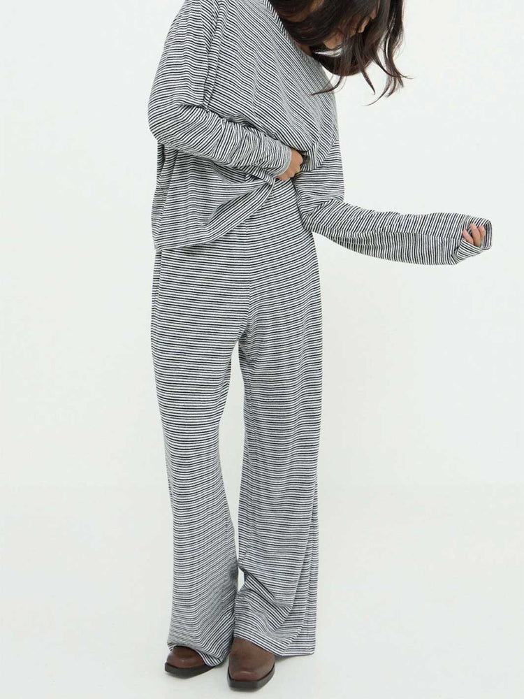 A person wearing a matching long-sleeve top and wide-leg pants set with thin horizontal gray and white stripes, shown against a plain white studio background.