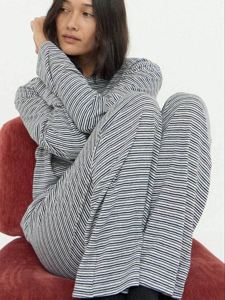 A model wearing a matching black and white striped lounge set, sitting on a red velvet armchair against a plain white background.