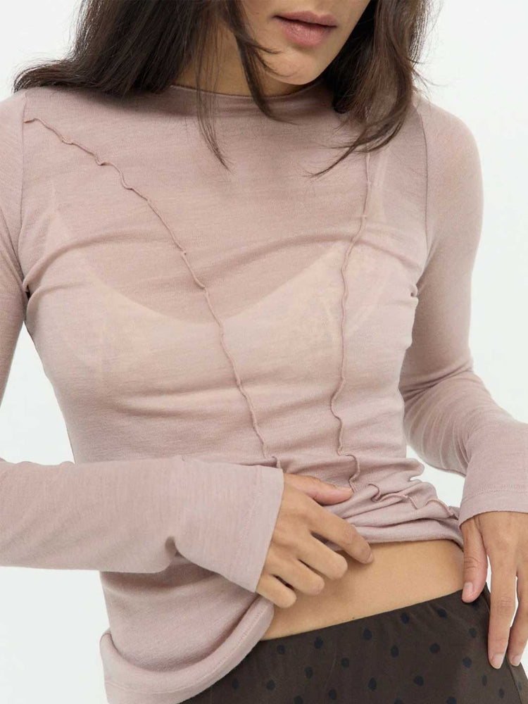 A close-up of a woman wearing a fitted, long-sleeve dusty pink top with a unique crinkled or pleated texture across the chest and shoulders, paired with dark brown polka-dot bottoms.