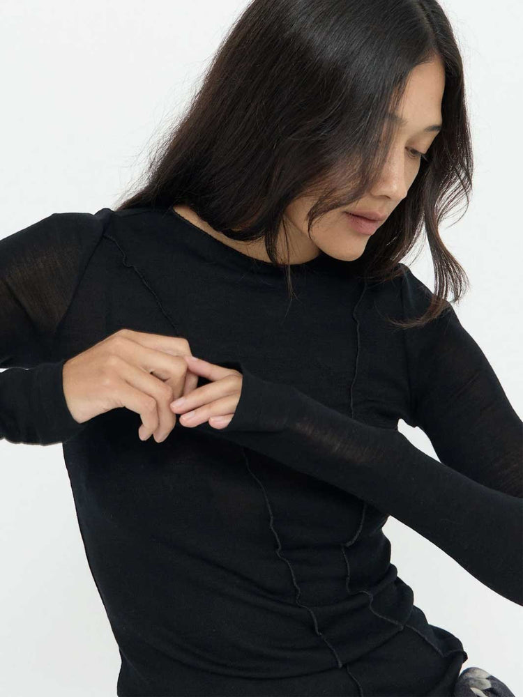 A woman wearing a black long-sleeve ribbed top with sheer mesh sleeves, shown from the chest up against a plain light background.