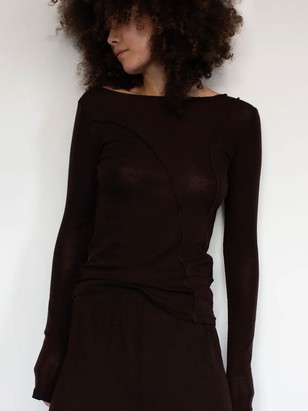 Woman wearing a dark brown long-sleeve Merino knit top against a white background