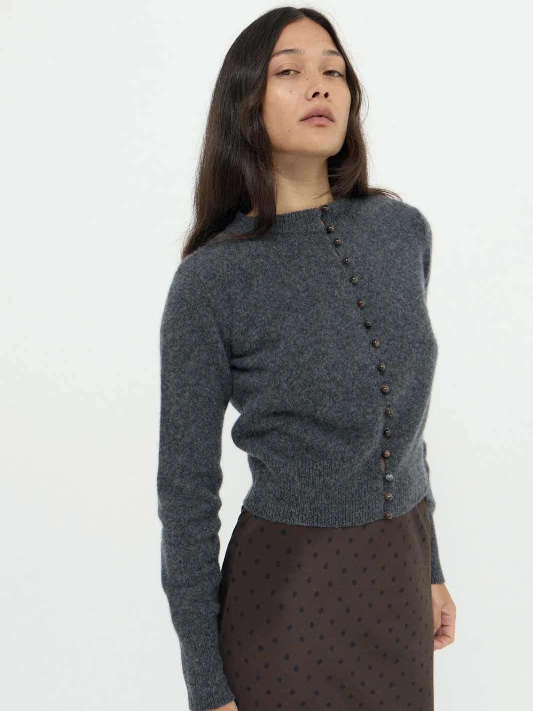 A woman wearing a dark gray knit cardigan with a buttoned front and a brown polka-dot skirt, photographed against a plain light background.