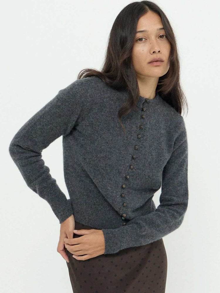 A woman wearing a dark gray knit cardigan sweater with a buttoned front and a brown polka-dot skirt, photographed against a plain white studio background.