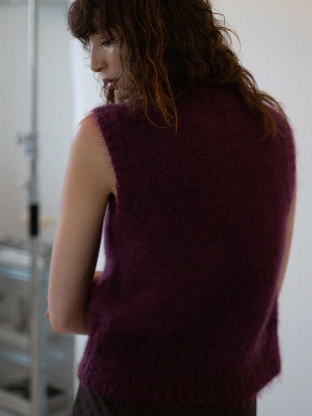Person wearing a purple sleeveless sweater against a neutral background