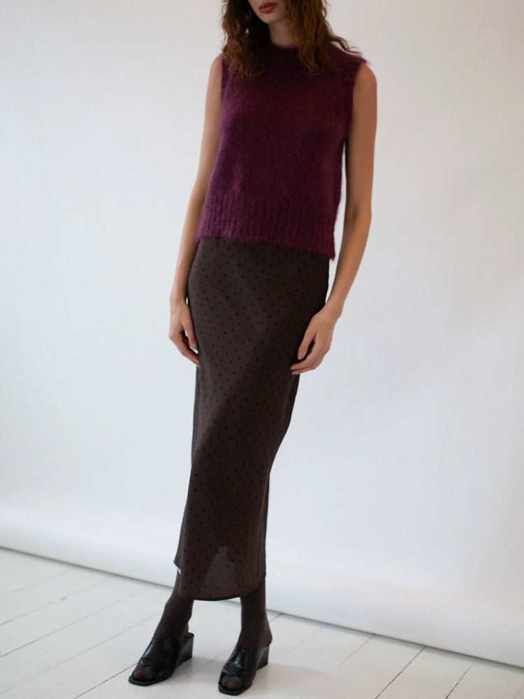 Person wearing a dark purple sleeveless top and brown patterned skirt against a white background