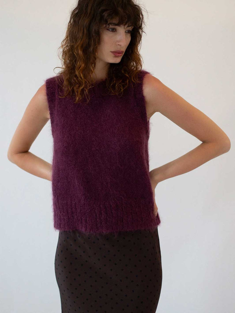 Woman wearing a purple sleeveless knitted top against a white background