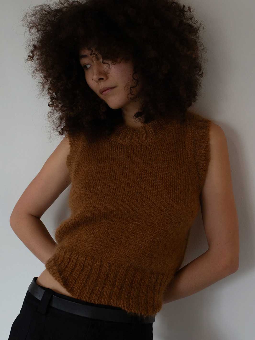 Person wearing a brown knitted sleeveless sweater against a plain background