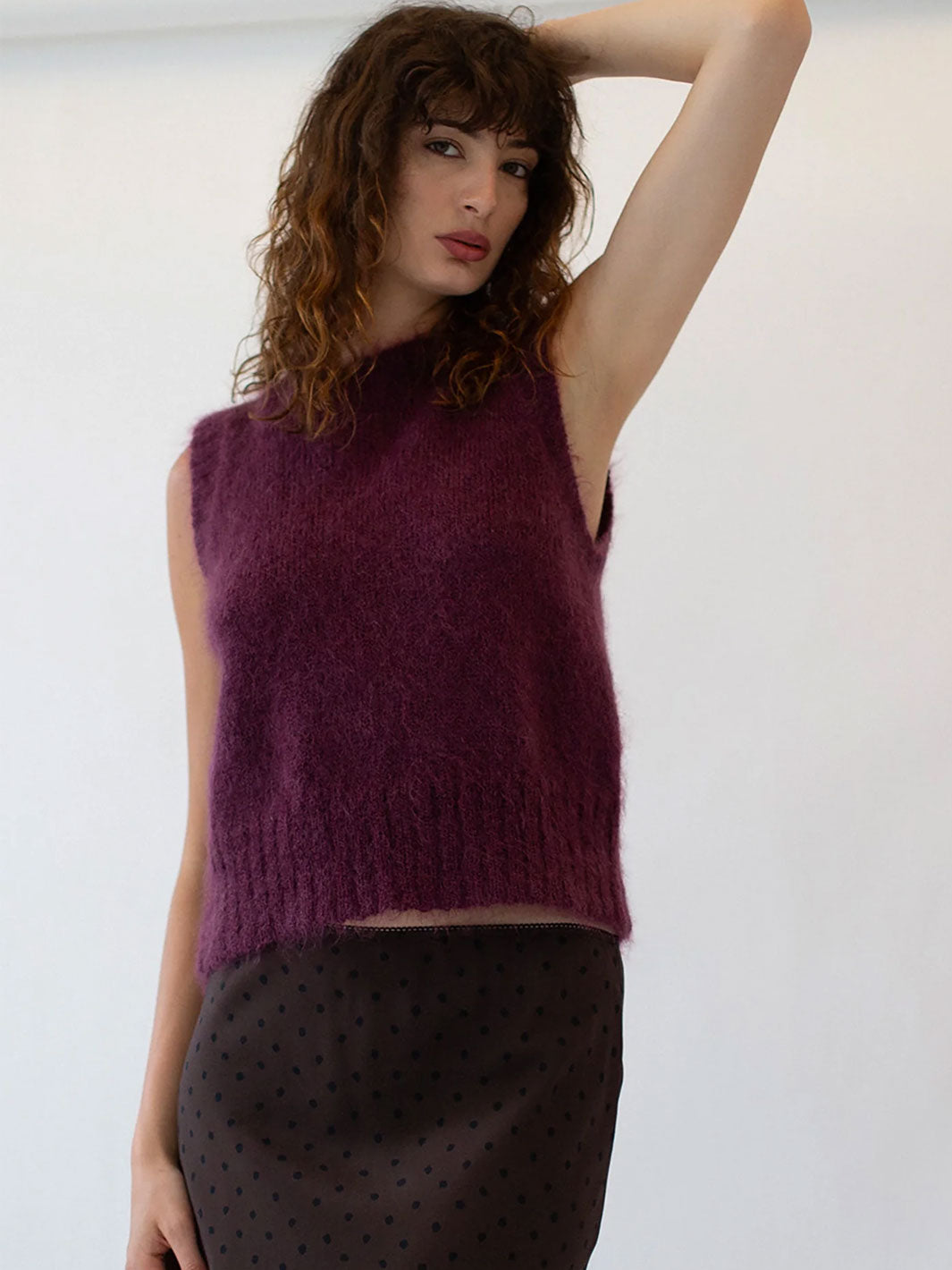 Woman wearing a purple sleeveless knitted top against a white background