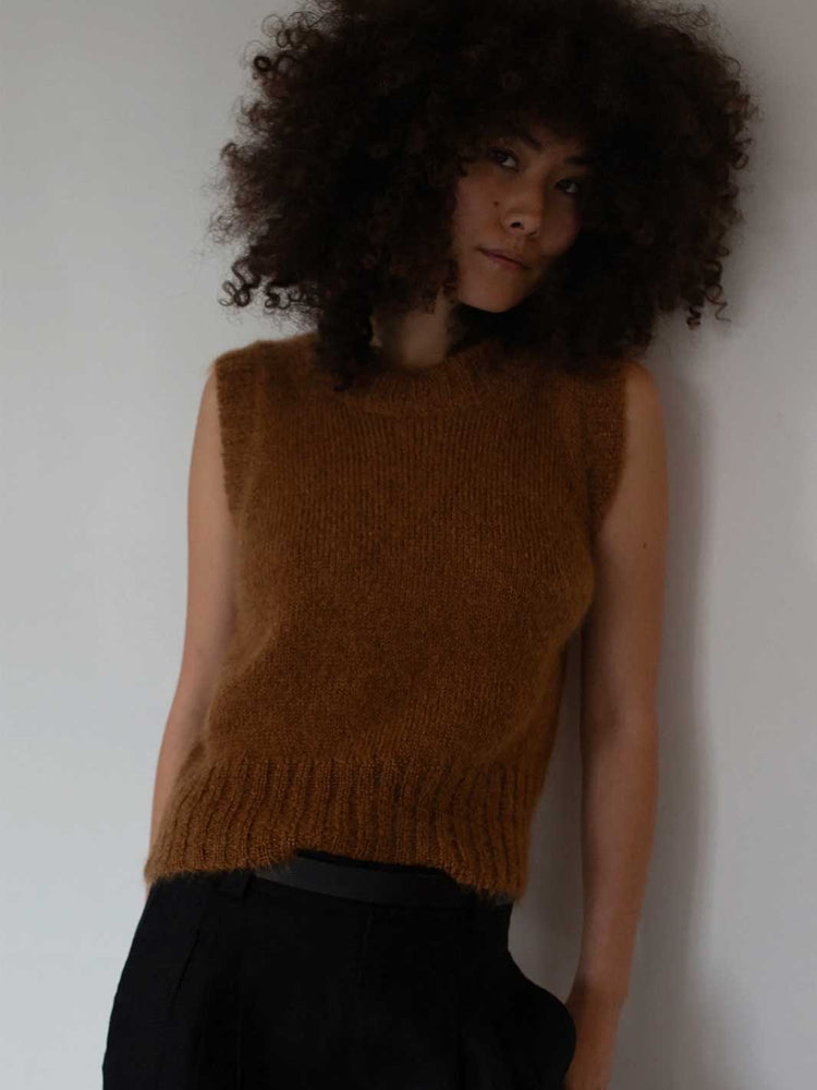 Woman wearing a brown knitted sleeveless top against a plain background