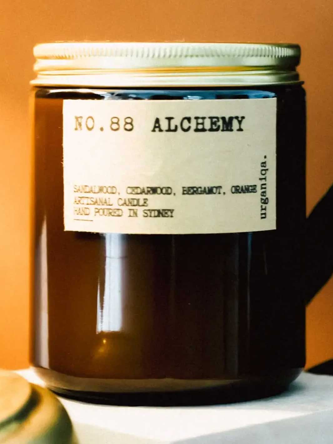 A dark amber glass jar candle with a cream paper label reading &