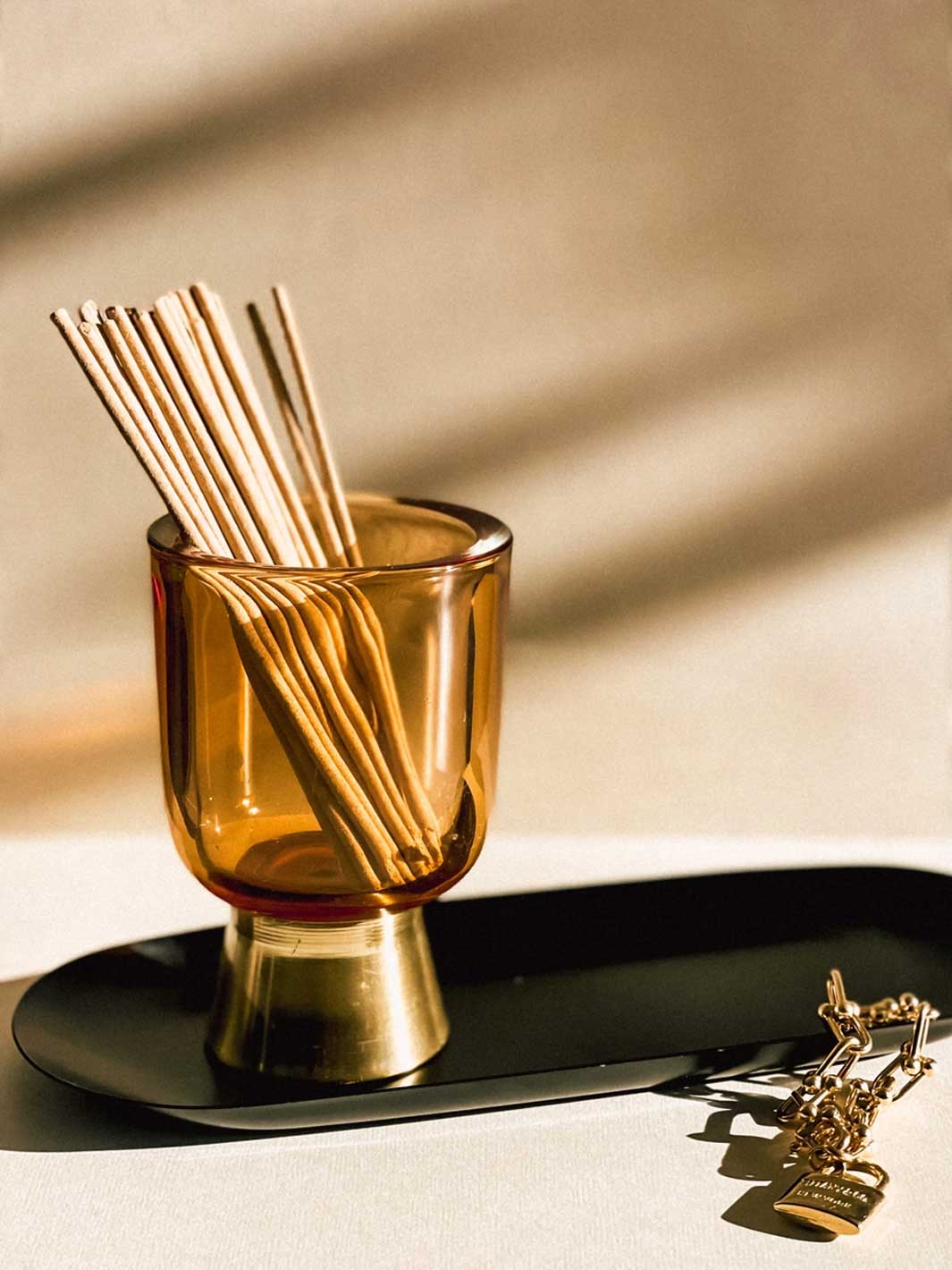 Amber glass holder with incense sticks on a black tray against a beige background