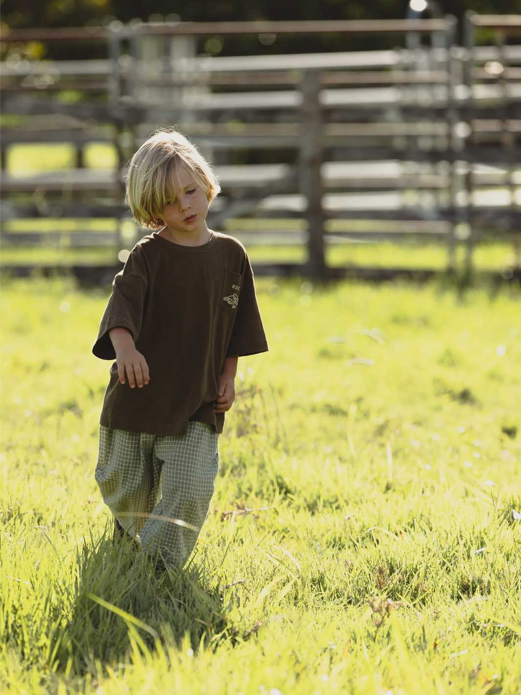 Child standing in a grassy field with wooden fences in the background