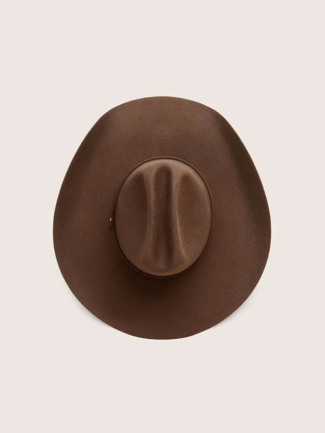 A brown wide-brim cowboy hat photographed from directly above on a light beige background.