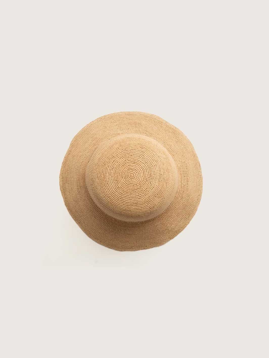 A top-down view of a light beige straw sun hat on a solid off-white background.