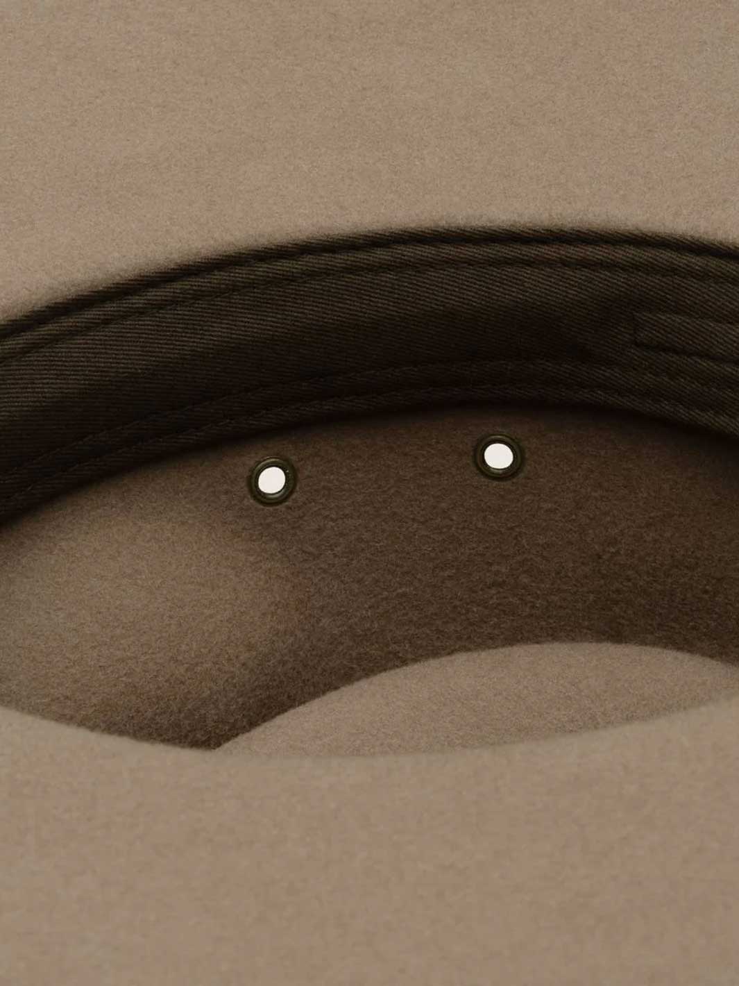 Close-up detail of a beige felt hat showing the dark brown stitched brim edge and two small metallic eyelets.