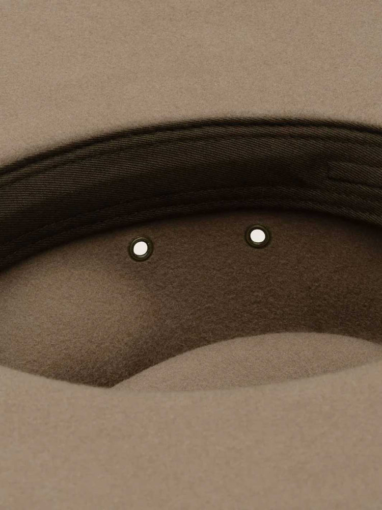Close-up detail of a beige felt hat showing the dark brown stitched brim edge and two small metallic eyelets.