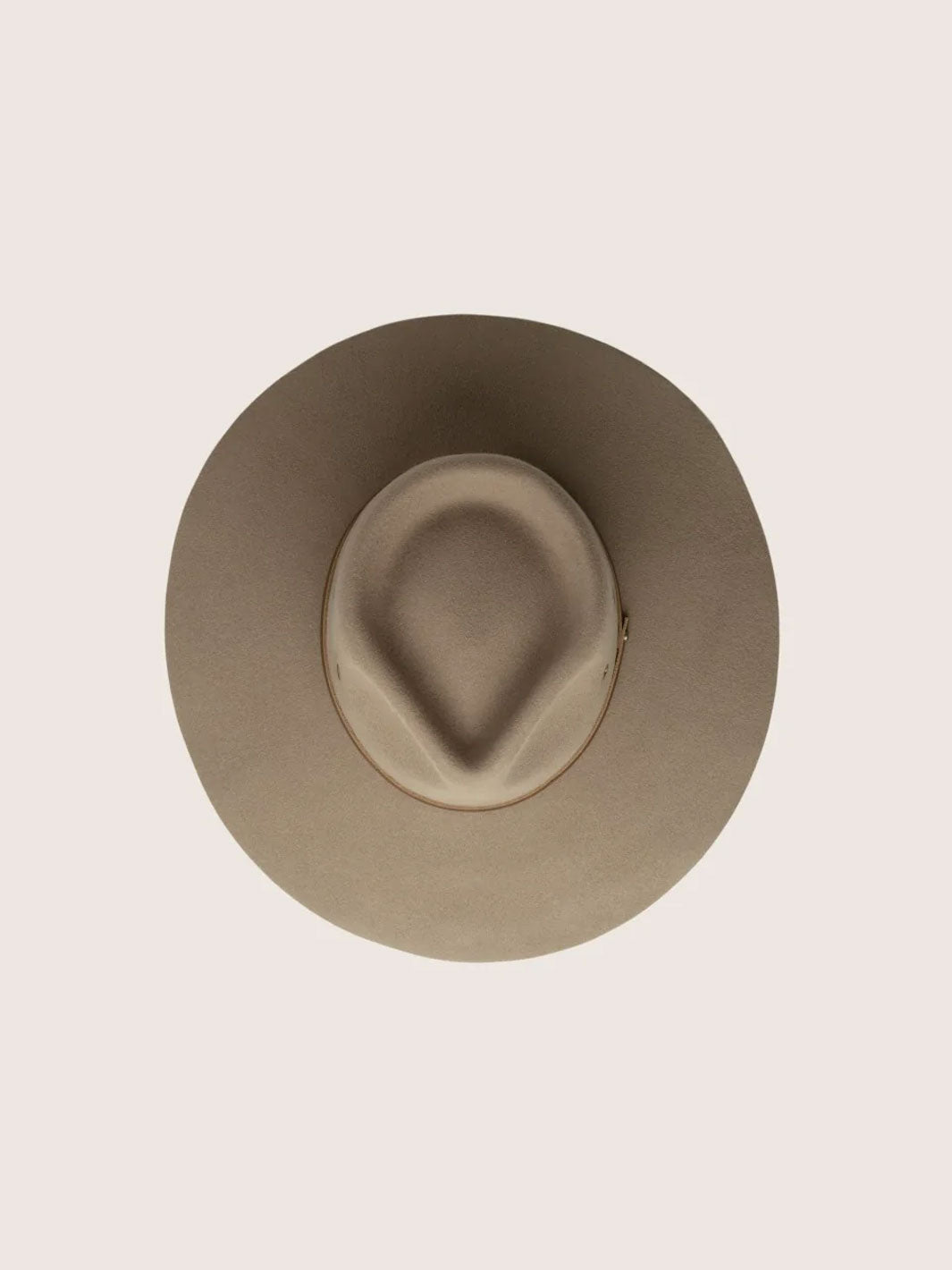 A top-down view of a wide-brim outback hat in a light taupe-beige colour, centred on a solid pale pinkish-beige background.