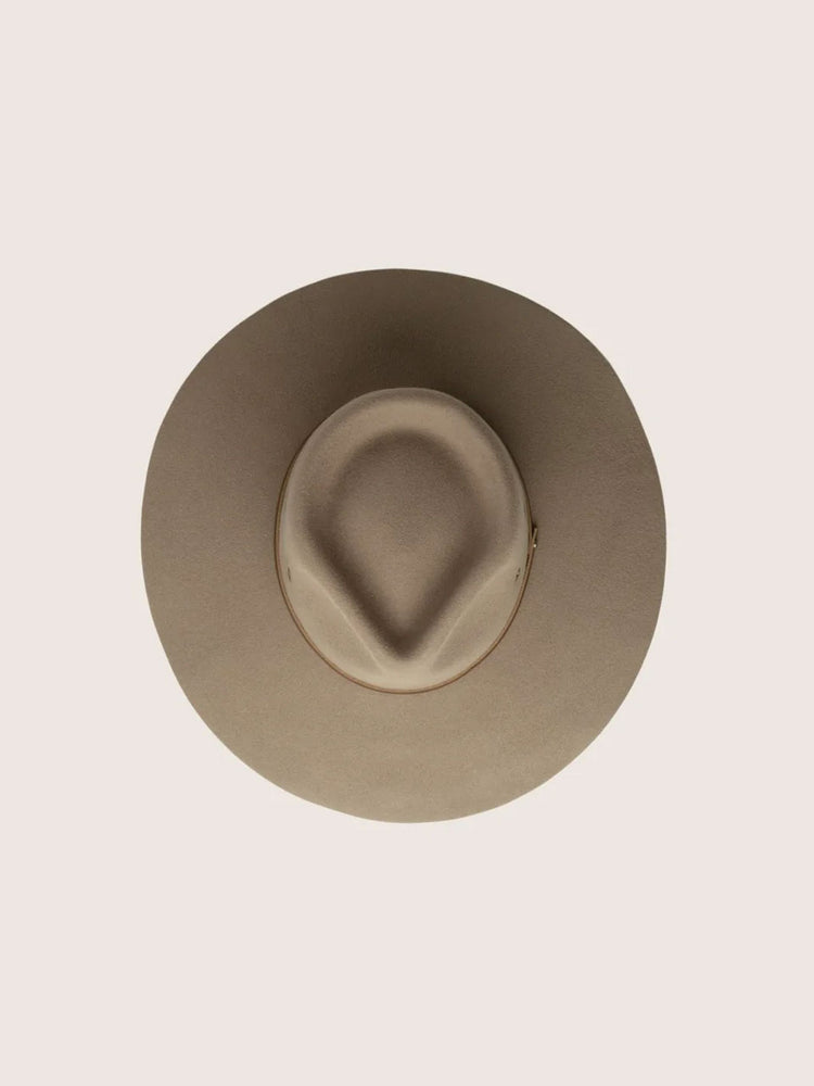 A top-down view of a wide-brim outback hat in a light taupe-beige colour, centred on a solid pale pinkish-beige background.